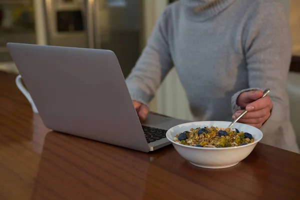 Mujer desayunando mientras usa el portátil — Foto de Stock
