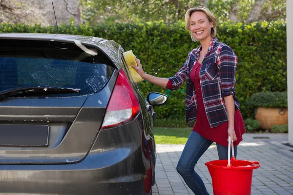 Mulher sorridente limpando seu carro com esponja — Fotografia de Stock