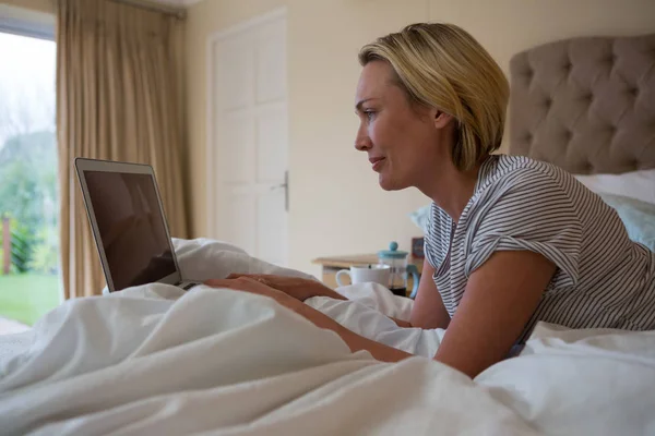 Mujer usando el ordenador portátil mientras se relaja en la cama — Foto de Stock