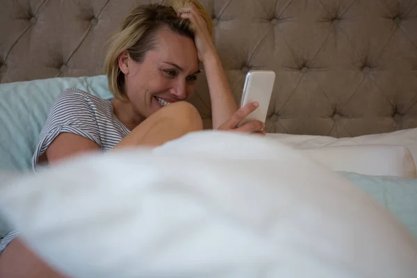 Woman using phone while relaxing on bed — Stock Photo, Image