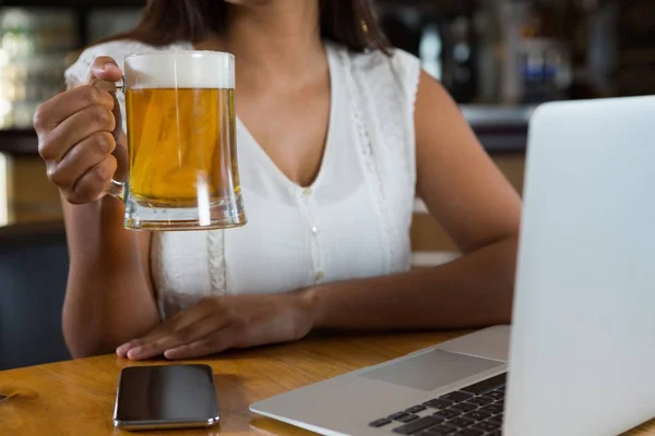 Mulher segurando copo de cerveja no bar — Fotografia de Stock
