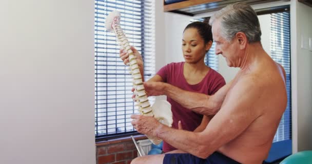 Fisioterapeuta explicando el modelo de columna vertebral al paciente mayor — Vídeos de Stock