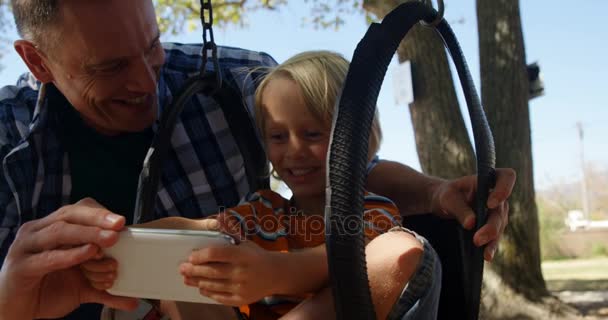 Батько і син використовують цифровий планшет на дитячому майданчику — стокове відео