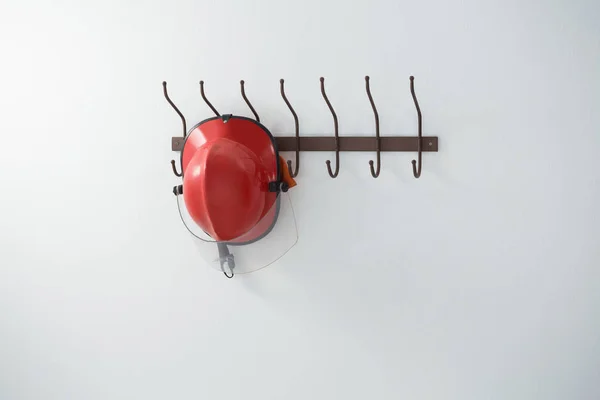 Red hardhat hanging on hook — Stock Photo, Image