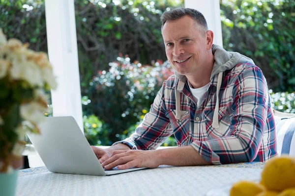 Усміхнений чоловік використовує ноутбук у ганку — стокове фото