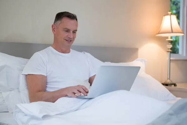 Homem usando laptop na cama no quarto — Fotografia de Stock