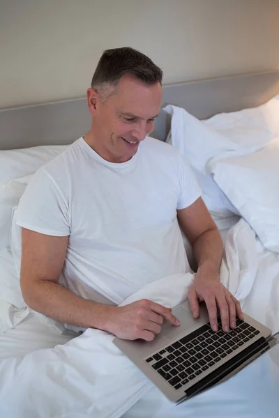 Чоловік використовує ноутбук на ліжку в спальні — стокове фото