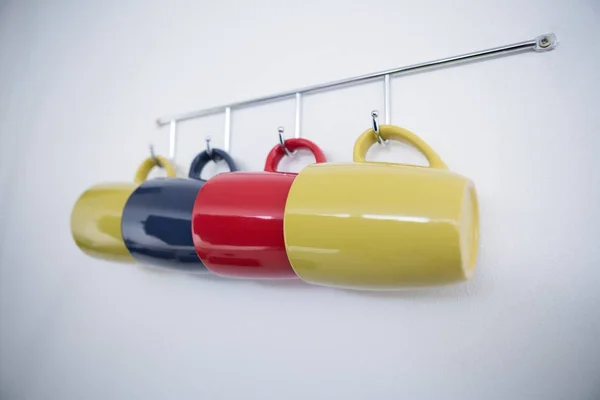 Colorful mugs hanging on hook — Stock Photo, Image