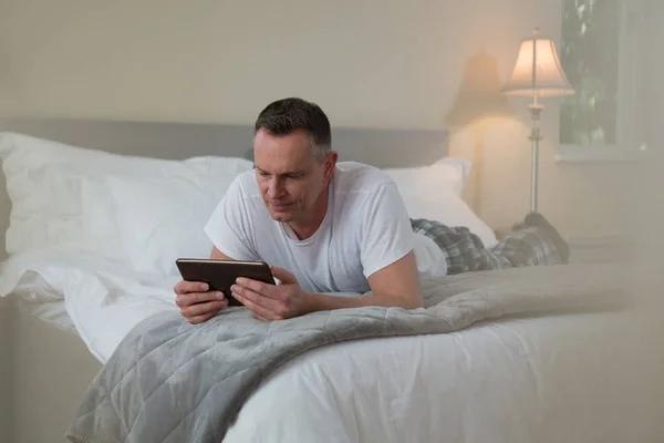 Uomo sdraiato sul letto e utilizzando tablet — Foto Stock