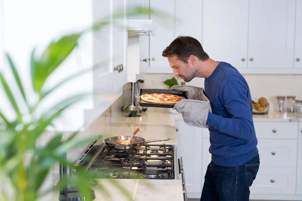 Hombre oliendo pizza horneada en la cocina —  Fotos de Stock