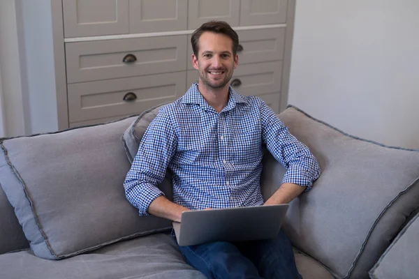 Homem usando laptop enquanto relaxa no sofá — Fotografia de Stock