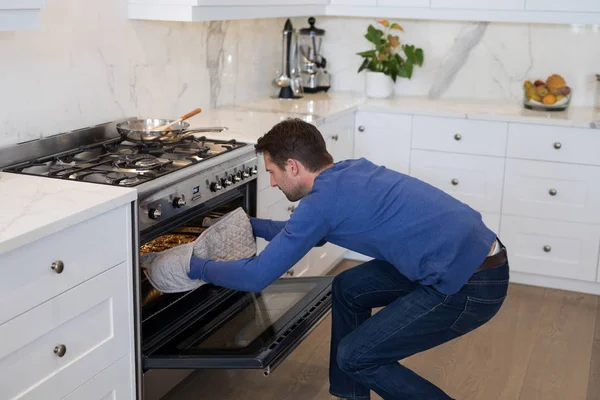 Hombre poniendo pizza en el horno en la cocina —  Fotos de Stock