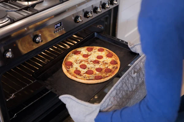 Man putting pizza into oven in kitchen — Stock Photo, Image