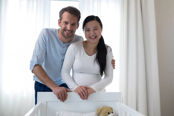 Couple heureux debout près de lit bébé — Photo