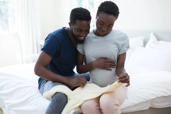 Couple holding baby clothes in bedroom — Stock Photo, Image