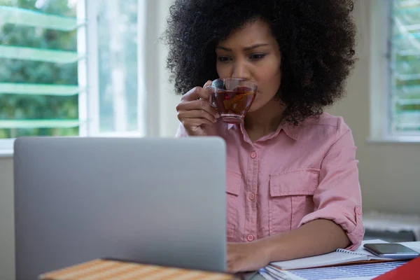 Frau trinkt Zitronentee, während sie Laptop benutzt — Stockfoto