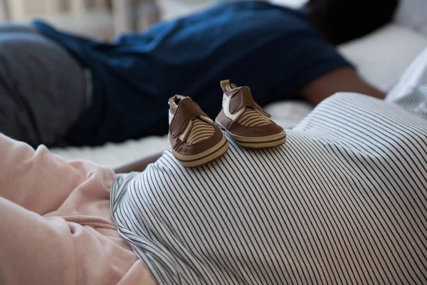 Pregnant woman relaxing with baby shoes — Stock Photo, Image