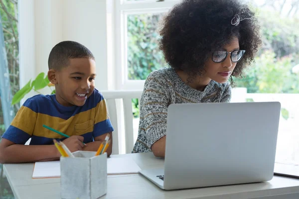 Син дозує домашнє завдання, поки мати використовує ноутбук — стокове фото