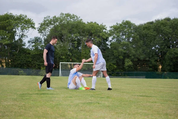 Fotbollsspelare hjälpa sin vän att få upp — Stockfoto