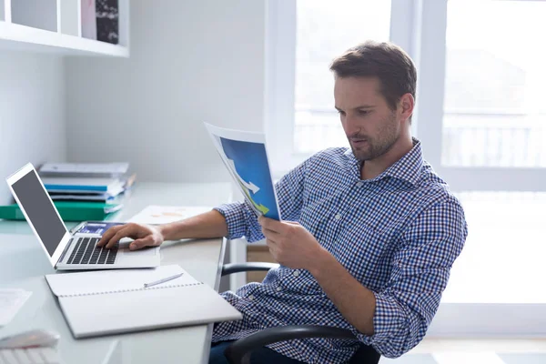 Hombre mirando gráfico mientras usa el ordenador portátil — Foto de Stock