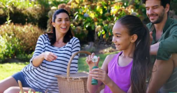 Girl Blowing Bubble While Her Parents Sitting Background Park — Stock Video