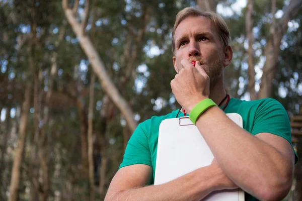 Athletic coach blowing whistle in forest — Stock Photo, Image