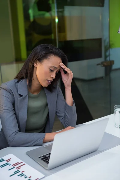 Verkrampte zakenvrouw met behulp van laptop aan balie — Stockfoto