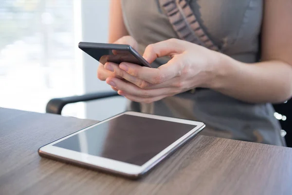 Vrouwelijke uitvoerend met behulp van telefoon aan tafel — Stockfoto