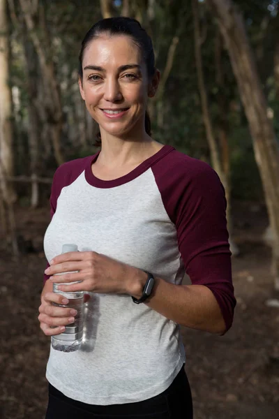 Kobieta stoi w lesie trzymając butelkę wody — Zdjęcie stockowe
