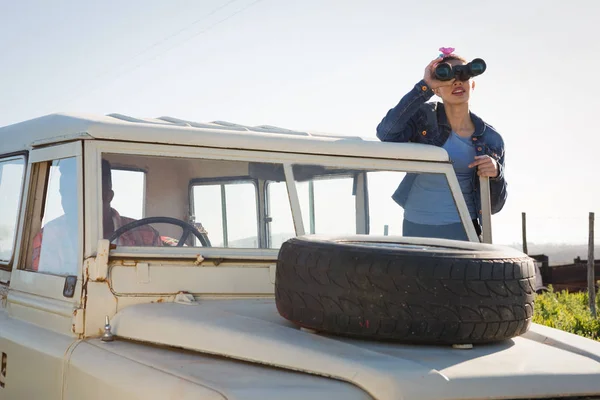 Woman looking through binoculars at countryside — Stock Photo, Image