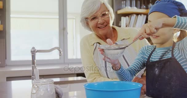 小麦粉と のキッチンで彼女を見ておばあちゃんをふるうシェフ キャップを持つ少女 — ストック動画