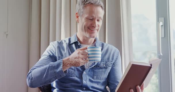 Mann Liest Buch Während Hause Kaffee Trinkt — Stockvideo