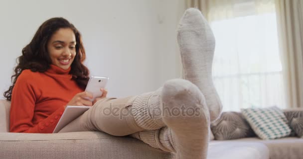 坐在沙发上的女人在家里用手机笑着4K — 图库视频影像