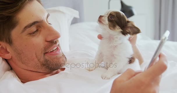 男子躺在床上抚摸他的小狗 而使用手机在卧室4K — 图库视频影像