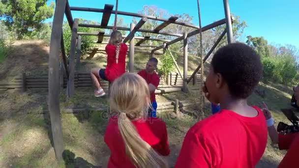 在阳光明媚的一天4K 的障碍课程中帮助学校的女孩攀爬绳索 — 图库视频影像