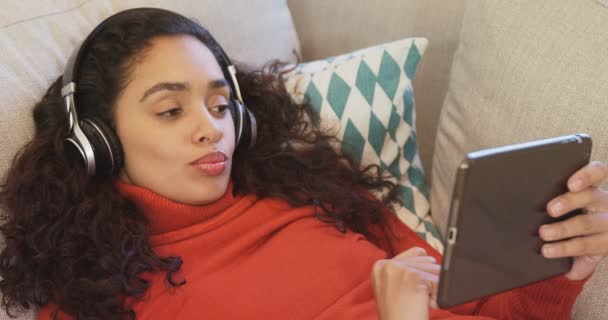 睡在沙发上的快乐女人特写用平板电脑在她的耳机上欣赏音乐4K — 图库视频影像