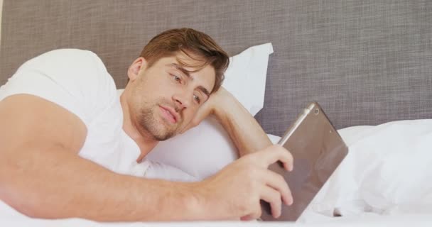 Sorrindo Homem Deitado Cama Usando Seu Tablet Digital Quarto — Vídeo de Stock