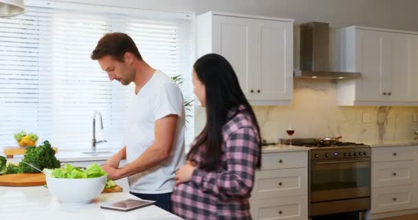 のキッチンで野菜を切断しながら男と話している妊娠女性 — ストック動画