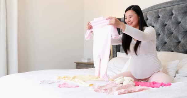 Femme Enceinte Souriante Tenant Des Vêtements Bébé Dans Chambre Coucher — Video