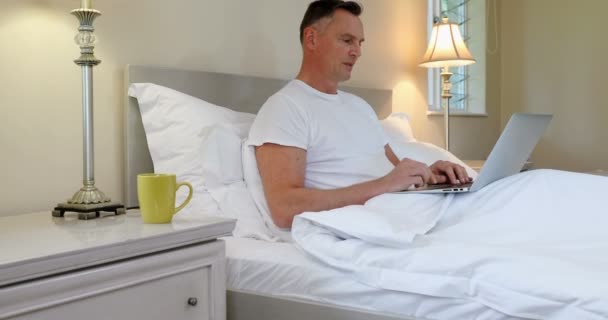 Hombre Usando Ordenador Portátil Mientras Relaja Cama Dormitorio — Vídeos de Stock