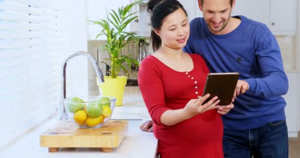 ホームの でキッチンでデジタル タブレットを使用して妊娠中のカップルの笑顔 — ストック動画