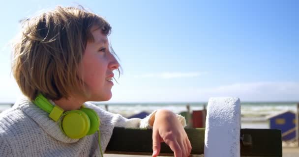 在阳光明媚的日子里 戴着耳机看海滩的少女4K — 图库视频影像