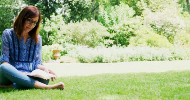 Ώριμη Γυναίκα Διαβάζοντας Ένα Βιβλίο Στον Κήπο Μια Ηλιόλουστη Ημέρα — Αρχείο Βίντεο