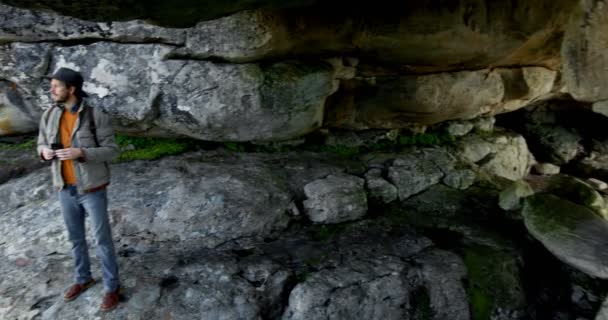 の田園地帯で洞窟近く双眼鏡でみる男性ハイカー — ストック動画