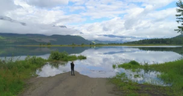 の田園地帯の湖の近くに立っている成熟した女性の空撮 — ストック動画