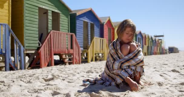 小女孩裹着毯子在沙滩上玩沙子4K — 图库视频影像