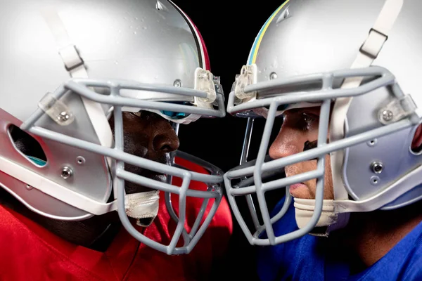 Side view close up of a Caucasian and an African American male American football player wearing their opposing team colours and helmets, standing opposite staring at each other, their helmets touching
