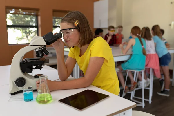 在科学课上 一个戴着安全眼镜 身穿黄色T恤的白人小学生坐在办公桌前 用显微镜的侧视图 — 图库照片