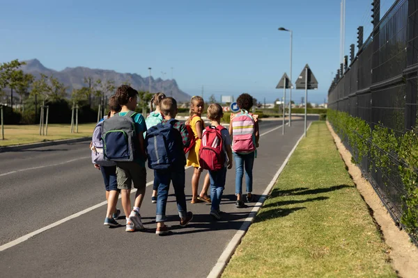 太陽の下で一緒に小学校への道を歩いて カメラに笑顔の多様なグループのフロントビュー — ストック写真