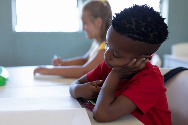 一个留着短发 穿着红色T恤 头枕在手上的书桌前 在小学课堂上边看他的书的非洲裔美国学生的侧影 — 图库照片